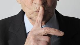 Пенсионер показывает жестом, что надо молчать