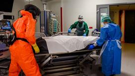 Медики в защитных костюмах перевозят каталку, накрытую простыней
