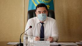 Нурлан Таубаев в маске сидит за столом