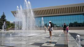 Люди гуляют вдоль фонтанов возле Дворца Республики в Алматы