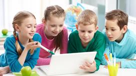 Девочки и мальчики в школе просматривают информацию с экрана ноутбука