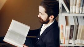 Бородатый мужчина в костюме сиди в библиотеке с книгой