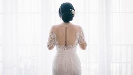 Невеста в свадебном платье стоит у окна