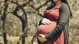 Беременная женщина держит руками живот
