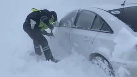 Полицейский откапывает машину из снега в ЗКО