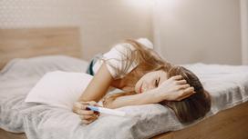 Девушка лежит на кровати с тестом на беременность