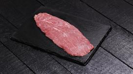 Кусок мяса лежит на деревянной кухонной доске