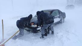 Мужчины толкают застрявшую в снегу машину