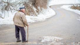 Пожилой человек идет по дороге с тростью
