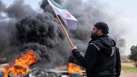 Сириец с флагом в руке на фоне подожженных шин