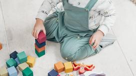Мальчик сидит на полу и составляет разноцветные кубики