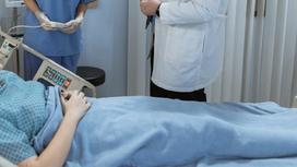 Женщина лежит на больничной койке, рядом стоят врачи