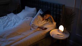 Женщина лежит в кровати и держит смартфон