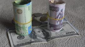 Свернутая пачка тенге стоит рядом со свернутой пачкой рублей на купюре доллара