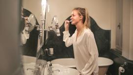 Девушка чистит зубы перед зеркалом