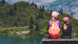 Две девочки сидят у озера в горах