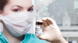 девушка в маске держит в руках ампулу с вакциной