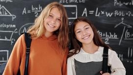 Две девочки-школьницы улыбаются, стоя у классной доски