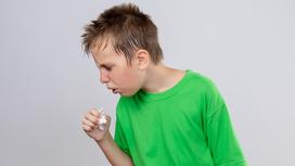 Мальчик в зеленой футболке кашляет