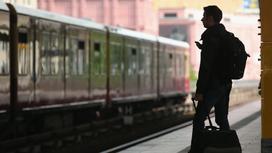 Мужчина с чемоданом на фоне отбывающего поезда