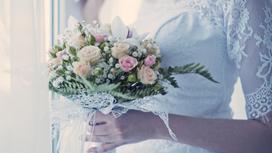 Невеста с букетом цветов стоит у окна