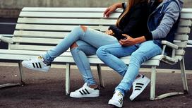 Парень и девушка в джинсах сидят полуобнявшись на лавочке