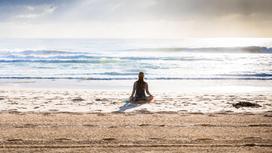 девушка сидит на берегу моря в позе лотоса