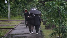 Девушки с зонтом идут по улице под дождем