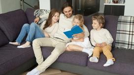 Родители с детьми читают книгу, сидя в гостиной на диване