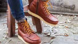 Кожаные коричневые ботинки на шнурках надеты на ноги в джинсах