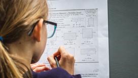 Девушка решает задачи по математике на листке бумаги
