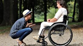 Парень сидит на корточках напротив девушки в инвалидной коляске