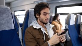 Бородатый мужчина сидит в поезде и держит в руках телефон