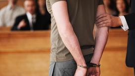 Мужчина в наручниках стоит в зале суда