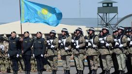 Люди в военной форме и с казахстанским флагом стоят в строю