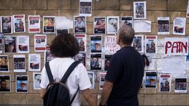 Люди смотрят на стену с фотографиями заложников, похищенных во время нападения ХАМАС