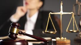 Женщина сидит за столом с атрибутами суда