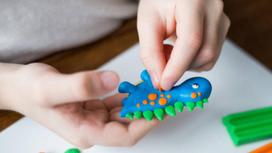 Ребенок лепит из пластилина фигурку динозаврика