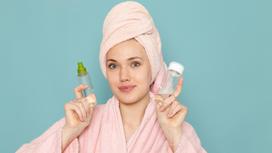 Девушка в халате и с полотенцем на голове держит косметические продукты