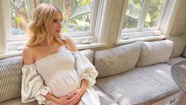 Беременная Эма Робертс сидит на диване
