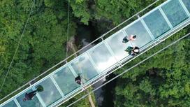 Туристы идут по стеклянному мосту