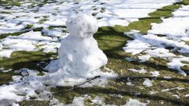 Снеговик стоит на фоне снега и травы