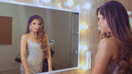Певица Нюша в блестящем платье смотрит в камеру через зеркало