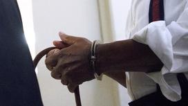 Мужчина держит в закованных в наручники руках трость