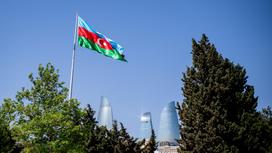 Флаг Азербайджана развевается на фоне зданий и деревьев