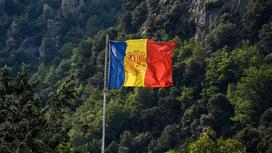 Флаг Андорры среди деревьев на фоне скал