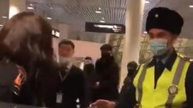 Женщина стоит перед полицейским в аэропорту Нур-Султана