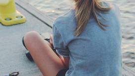 Девочка-подросток сидит возле реки