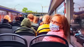 Женщина в маске смотрит в камеру в автобусе с людьми