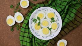 Половинки вареных яиц на тарелке и на столе с зеленью